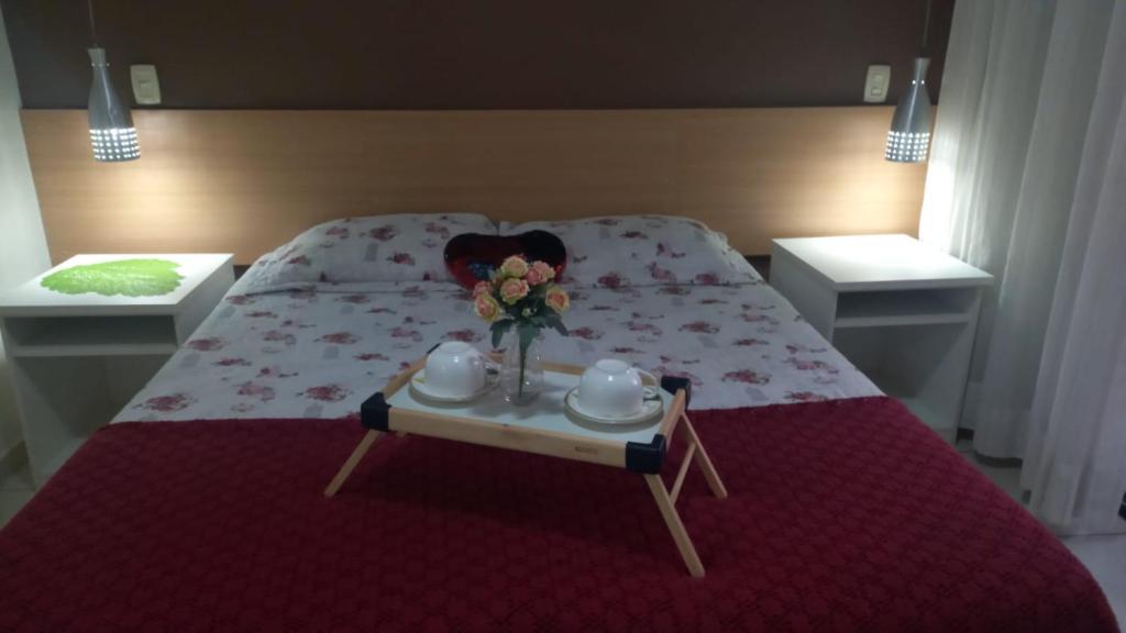 a bed with a table with a vase of flowers on it at Aconchegante Flat no Aldeia das Águas in Barra do Piraí
