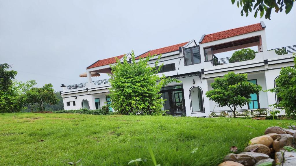 a large white building with a grass field in front of it at Mây Trắng Farmstay Villas Venuestay in Ba Vì