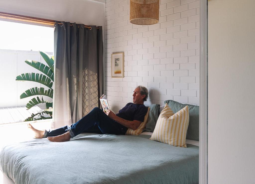 a man sitting on a bed reading a book at Pippi Beach Loft in Yamba