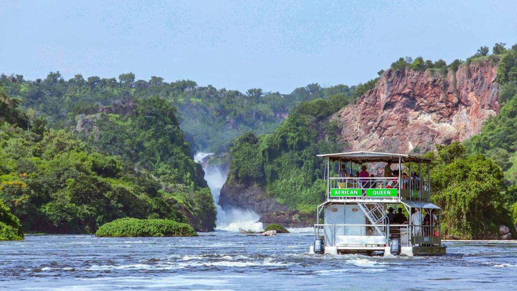 a tour boat on the river in front of a waterfall at Paraa Safari Lodge in Paraa