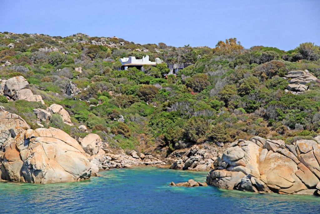 a house on a hill next to a body of water at Villa Eleonora - Sea view in Santa Teresa Gallura
