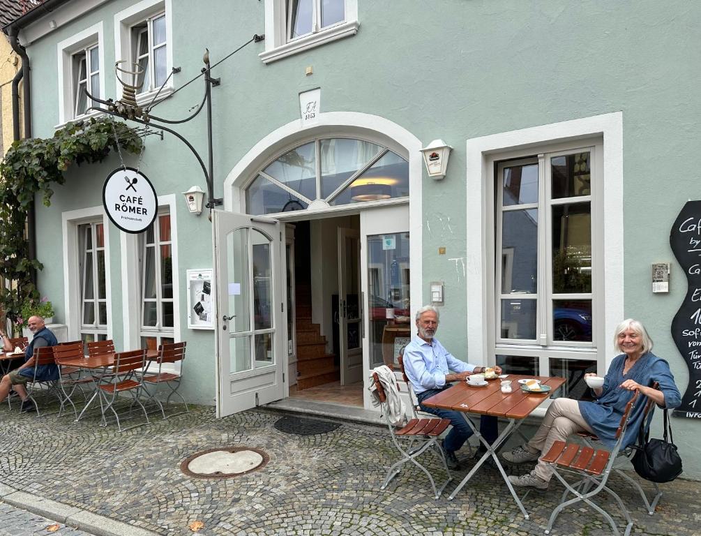 dos personas sentadas en una mesa fuera de un edificio en Vinopresso GmbH - Café Römer, en Prichsenstadt