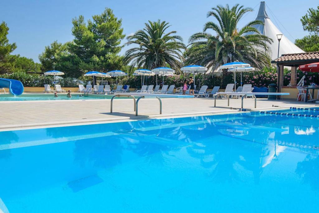 a swimming pool with chairs and umbrellas at ISA-Appartament standard 4 beds, air conditioning and private outdoor area in Village with 6 swimming-pools in Piombino