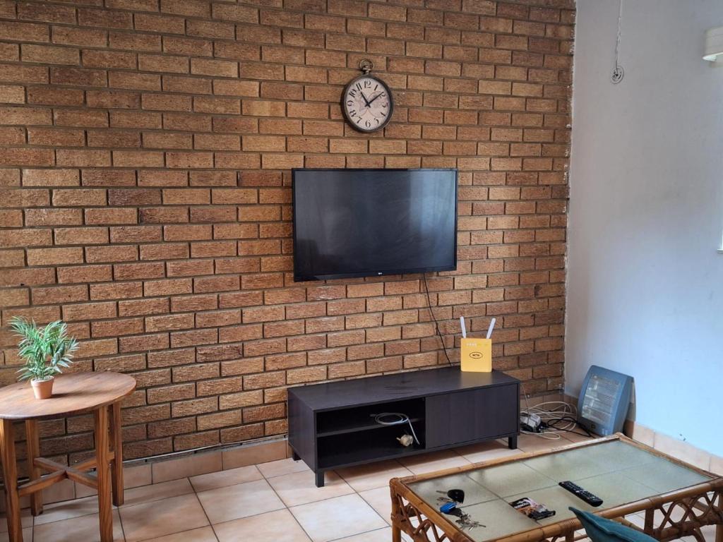 a living room with a brick wall with a tv at Warm, Comfy Duplex 5min Walk To North Park Mall in Pretoria