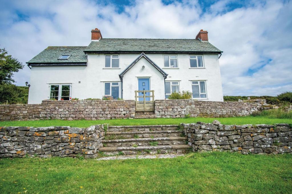 a white house behind a stone wall at Windy Walls - 3 Bedroom Holiday Home - Rhossili in Rhossili