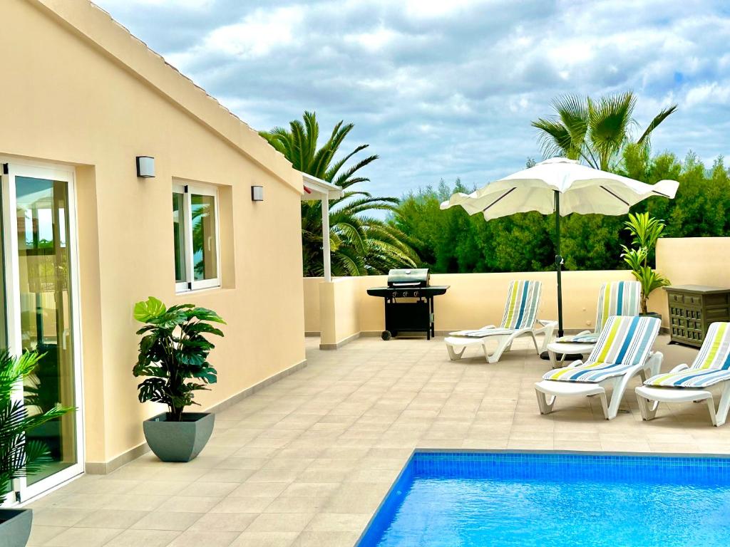 un patio con piscina, sillas y sombrilla en Villa Casa Sol, en Chayofa
