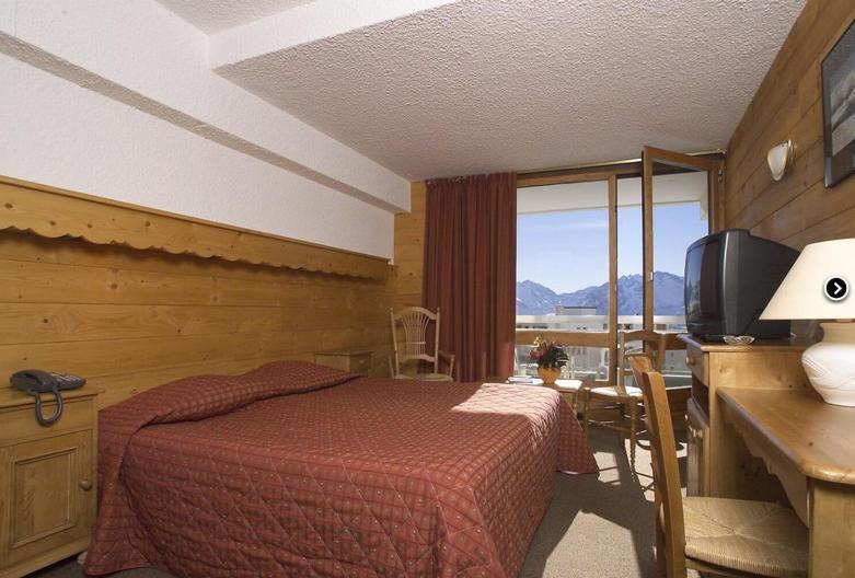 a bedroom with a bed and a television and a window at Hôtel Le Dôme in L&#39;Alpe-d&#39;Huez