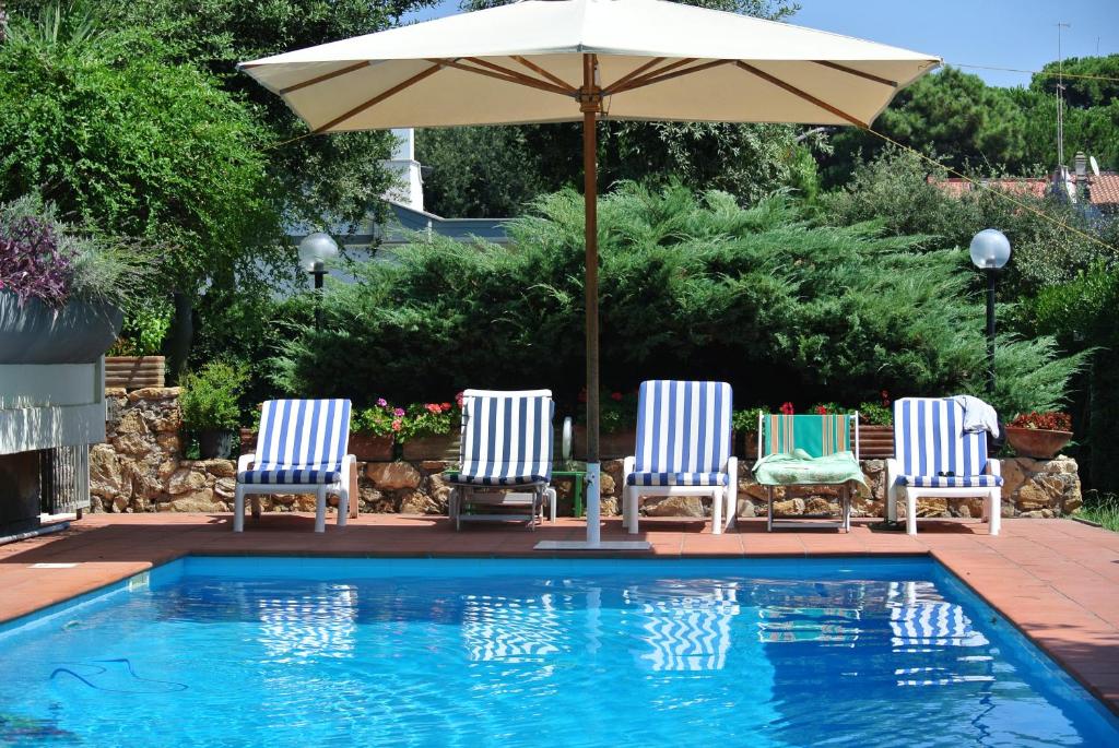 three chairs and an umbrella next to a swimming pool at Villa Marisa in Fregene