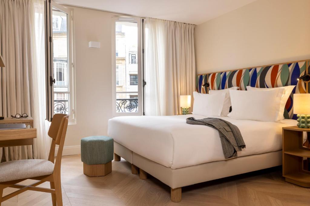 sypialnia z dużym białym łóżkiem i oknem w obiekcie Padam Hôtel w Paryżu