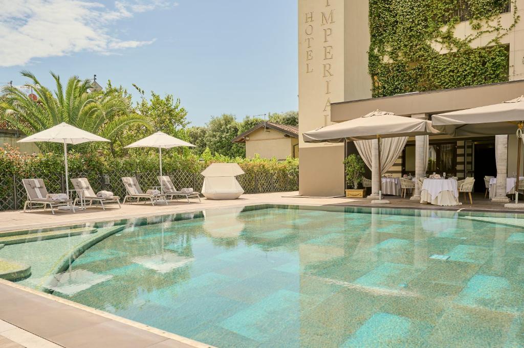 una piscina con sillas y sombrillas junto a un edificio en Grand Hotel Imperiale - Preferred Hotels & Resorts, en Forte dei Marmi