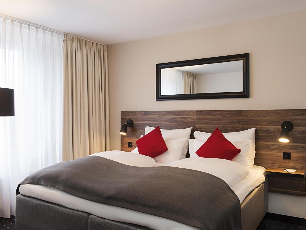 a hotel room with a large bed with red pillows at Victor's Residenz-Hotel München in Unterschleißheim