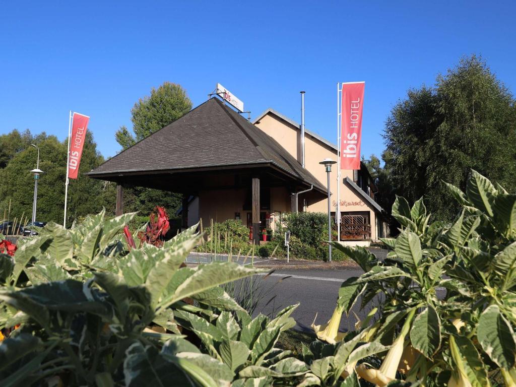 a building with red signs on the side of a road at ibis Egletons in Égletons