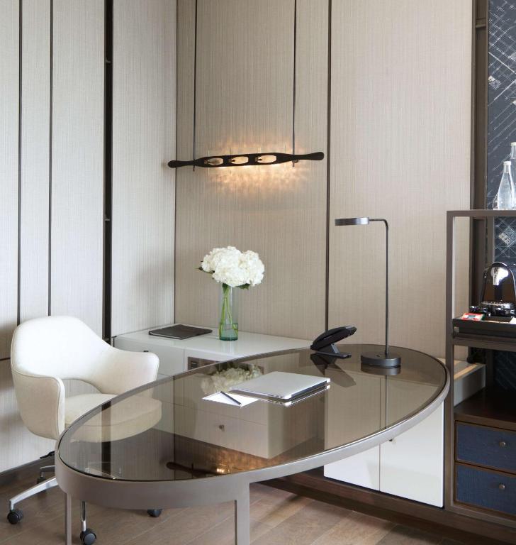 A polished glass-topped desk with office equipment and a lounge chair.