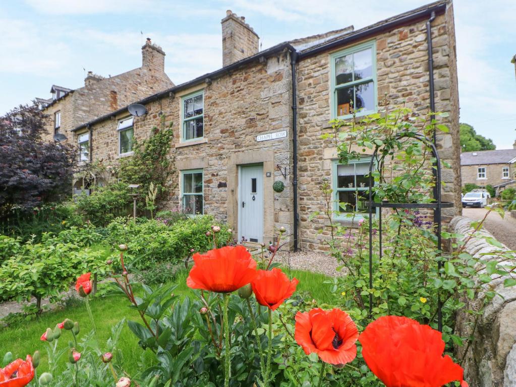 a stone house with red flowers in front of it at Chapel Cottage in Barnard Castle