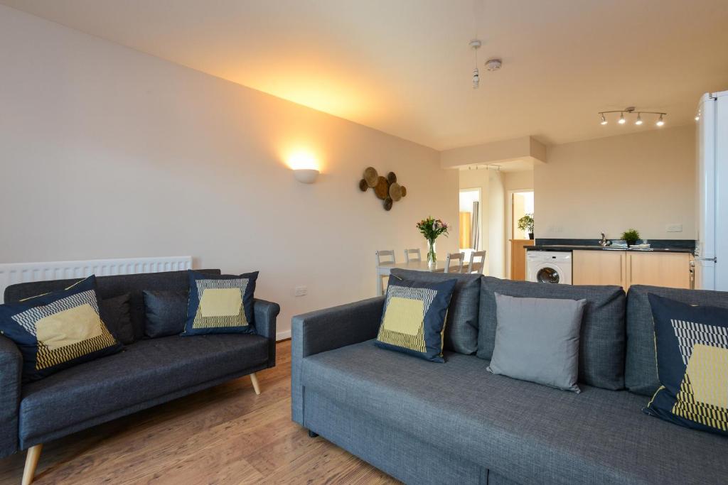 a living room with two blue couches and a kitchen at Portland Square - 2 Bedroom Modern City Apartment in Nottingham