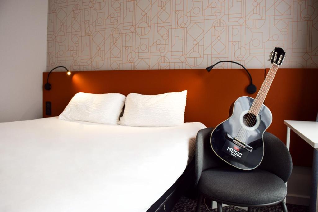 a guitar sitting on a chair next to a bed at ibis Rodez Centre in Rodez