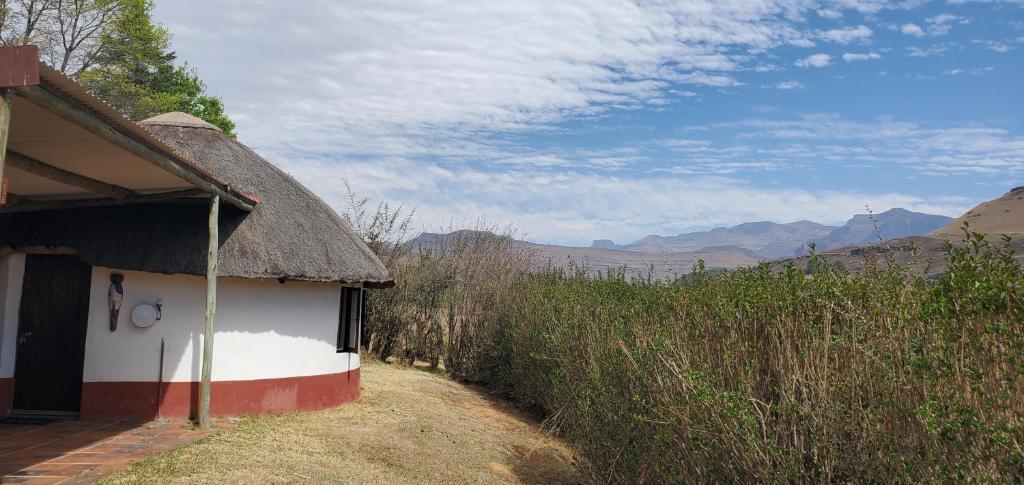 a house with a thatched roof next to a dirt road at Mashai Rest Rondavel in Underberg