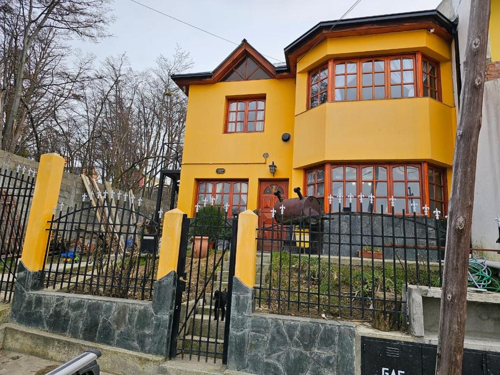 ein gelbes Haus mit roten Fenstern und einem Zaun in der Unterkunft La Herradura de Ushuaia in Ushuaia