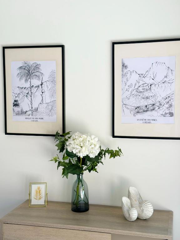 three framed drawings on a wall above a table with a vase of flowers at La Parenthèse chez Seb et Gwen in Le Tampon