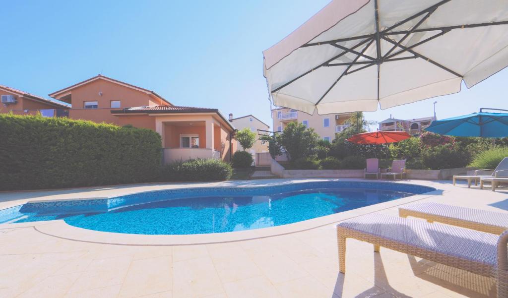 a swimming pool with an umbrella next to a house at Apartments Meri in Ližnjan