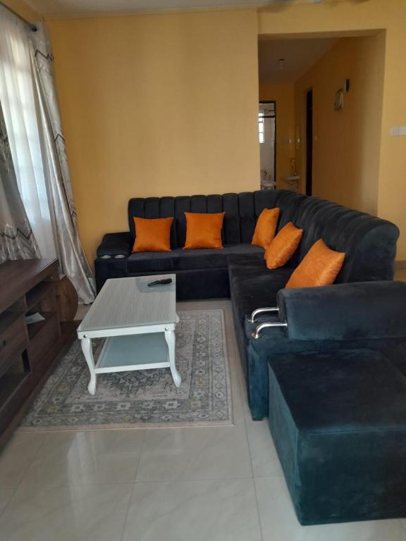 sala de estar con sofá negro y almohadas de color naranja en REHOBOTH'S APARTMENTS, en Kisumu
