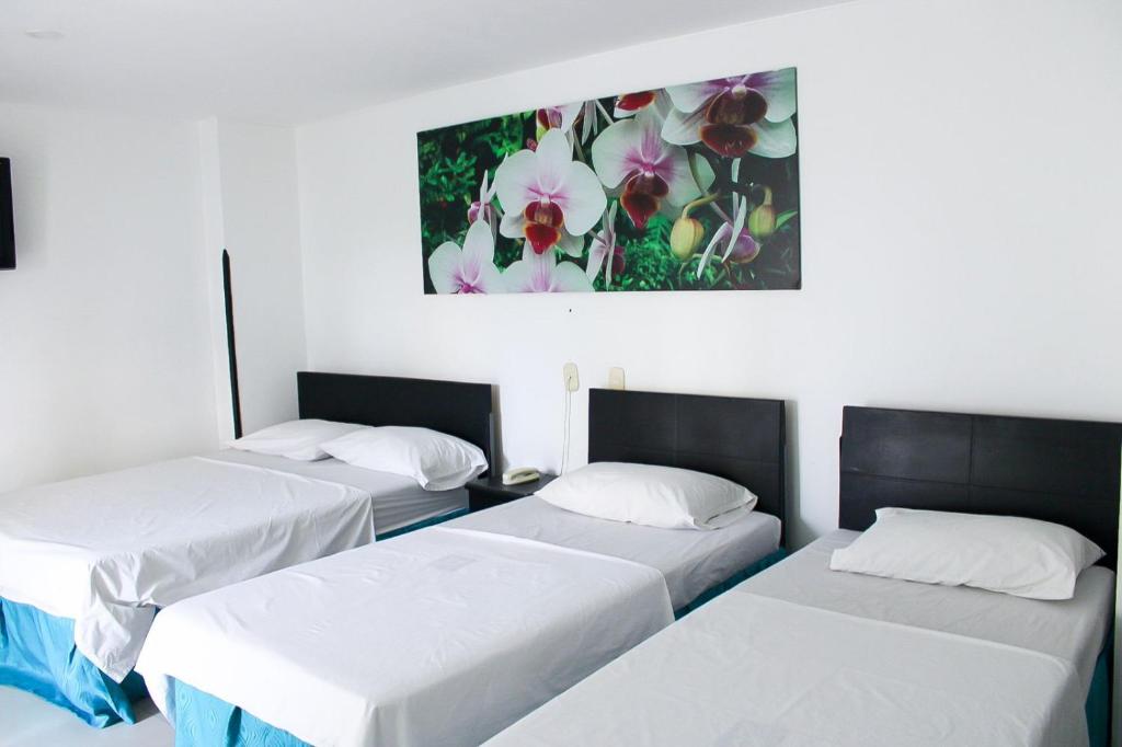 three beds in a room with a painting on the wall at Hotel Bucaramanga Plaza in Bucaramanga