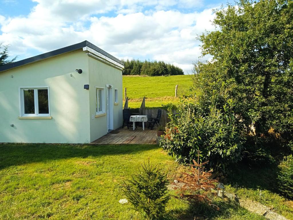una pequeña casa blanca en un campo con terraza de madera en La petite maison au calme dans les champs, en Matton-et-Clémency