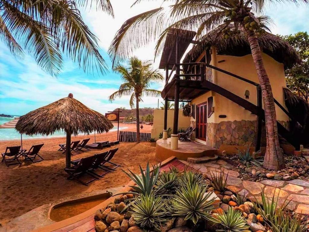 a building on a beach with palm trees and the ocean at Cabañas Punta Placer in San Agustinillo