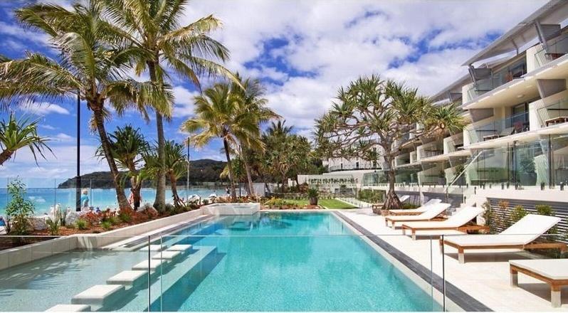 a swimming pool next to a resort with palm trees at Fairshore 22 Main Beach Views in Noosa Heads