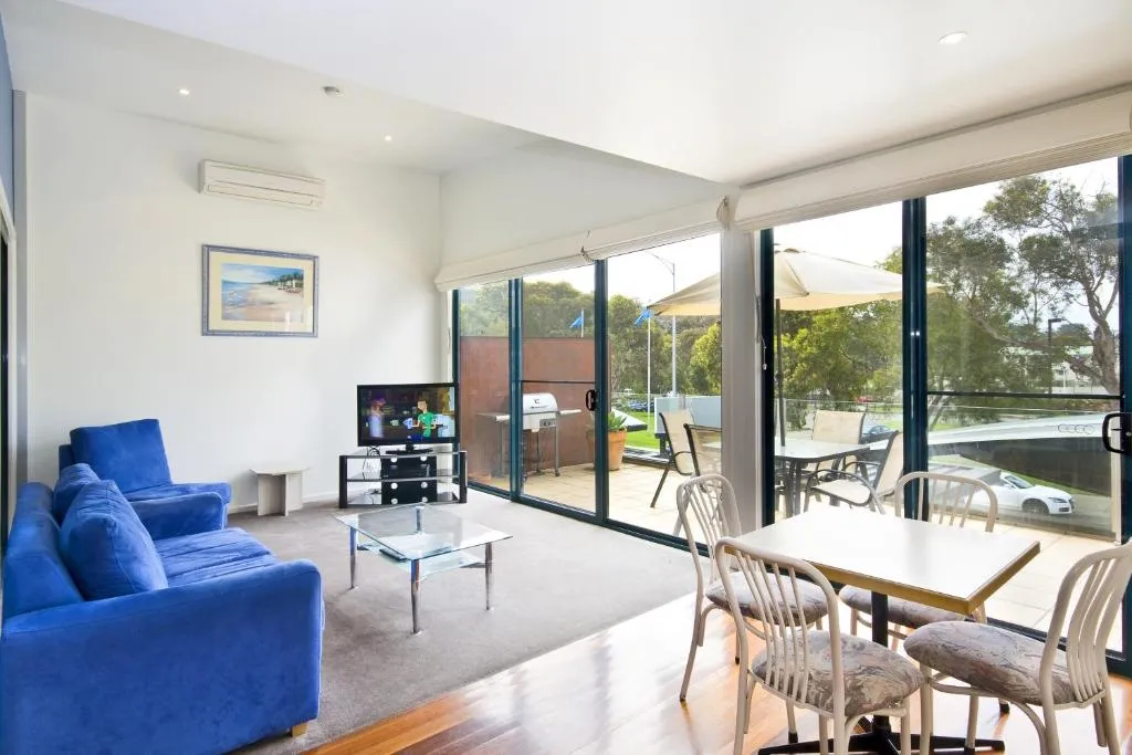 A living room with a blue sofa, a dining table and glass doors to a balcony