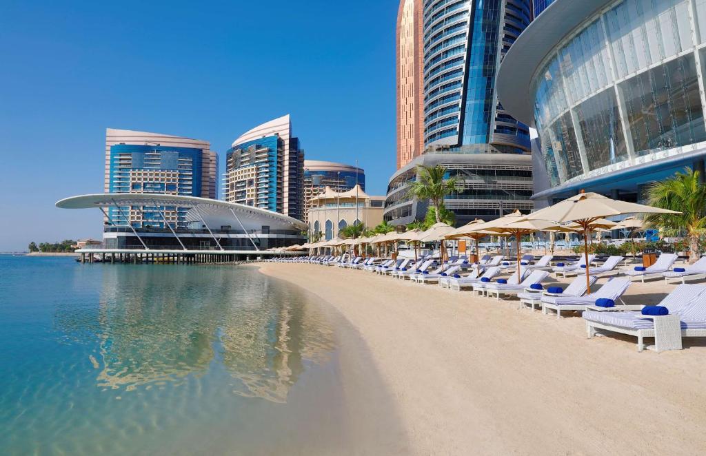 a beach with chairs and umbrellas in front of buildings at Conrad Abu Dhabi Etihad Towers in Abu Dhabi
