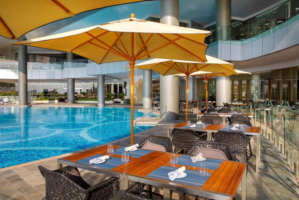 a restaurant with tables and umbrellas next to a swimming pool at Conrad Abu Dhabi Etihad Towers in Abu Dhabi