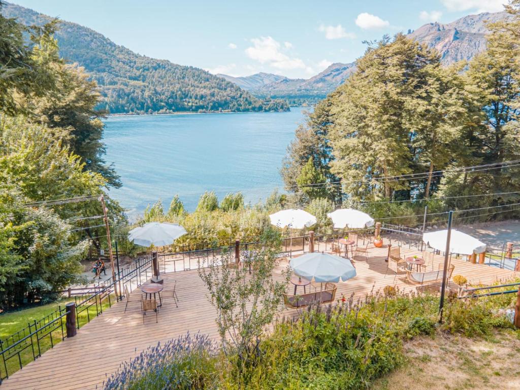 una terraza de madera con mesas y sombrillas junto a un lago en Hosteria El Condado by Nordic en San Carlos de Bariloche