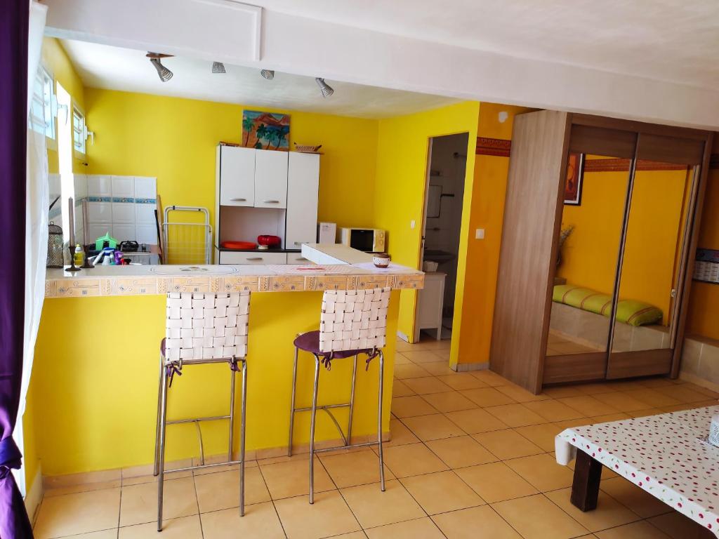 eine Küche mit gelben Wänden, einer Theke und Stühlen in der Unterkunft Gîtes TAINACO in Vieux-Habitants