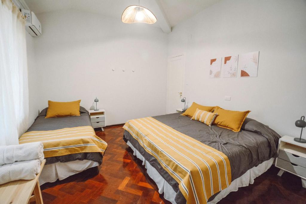 2 camas en una habitación con paredes blancas y almohadas amarillas en Anden Aristides en Mendoza