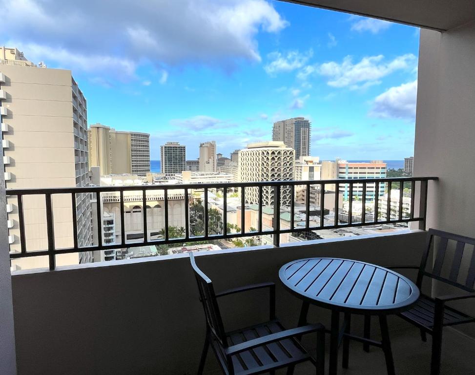 een balkon met een tafel en stoelen en uitzicht op de stad bij Royal Kuhio 1710 - Spacious Studio with Stunning Ocean City Views in the Heart of Waikiki! in Honolulu
