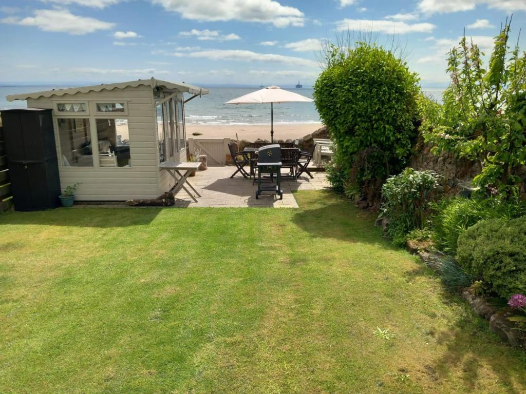 a garden with a table and an umbrella and the beach at Beachhaven116 Lovely beachside house Lower Largo in Lower Largo