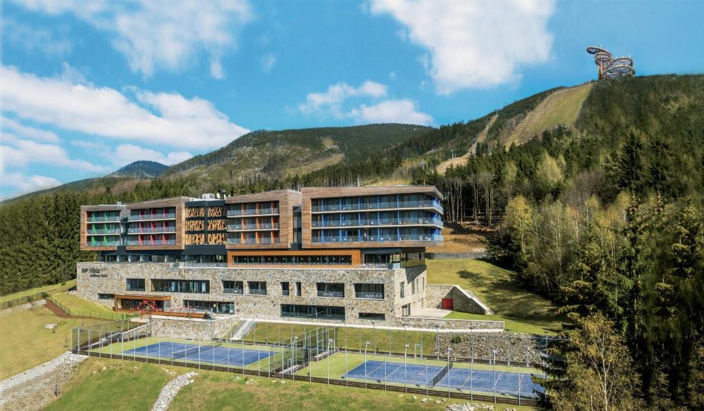 a building with tennis courts in front of a mountain at Wellness Hotel Vista in Dolní Morava