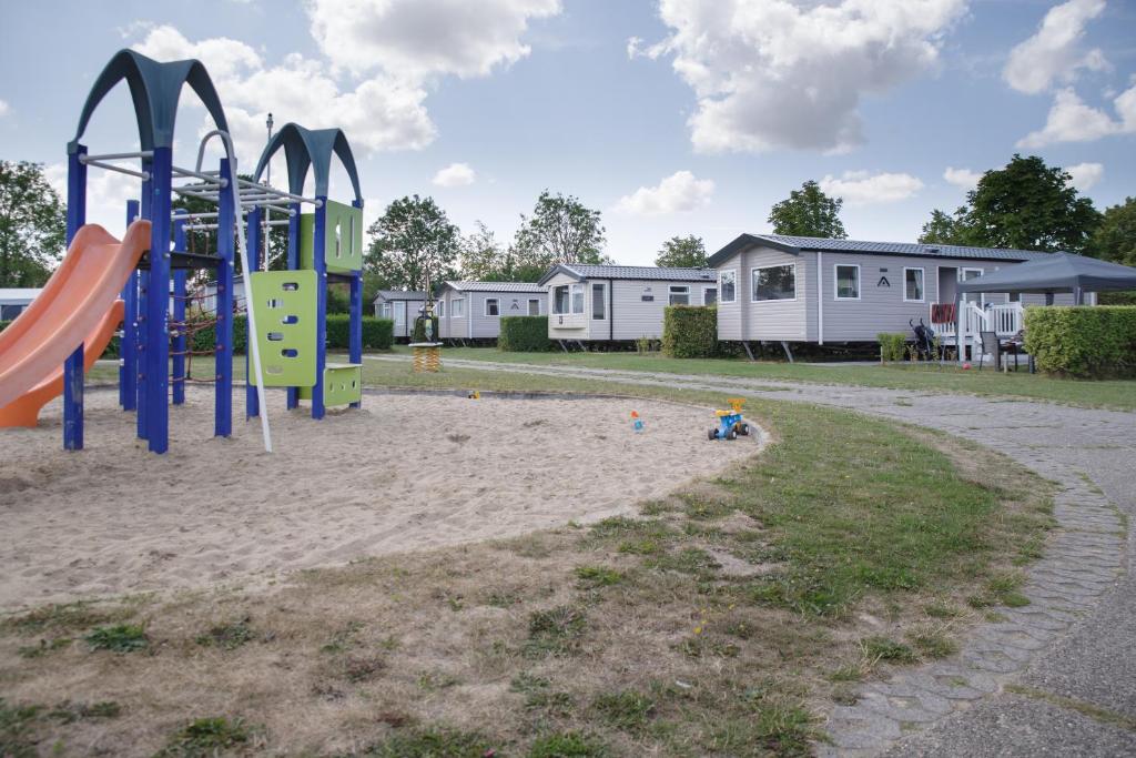un parque infantil en la arena con casas en el fondo en Camping 't Veerse Meer, en Wolphaartsdijk