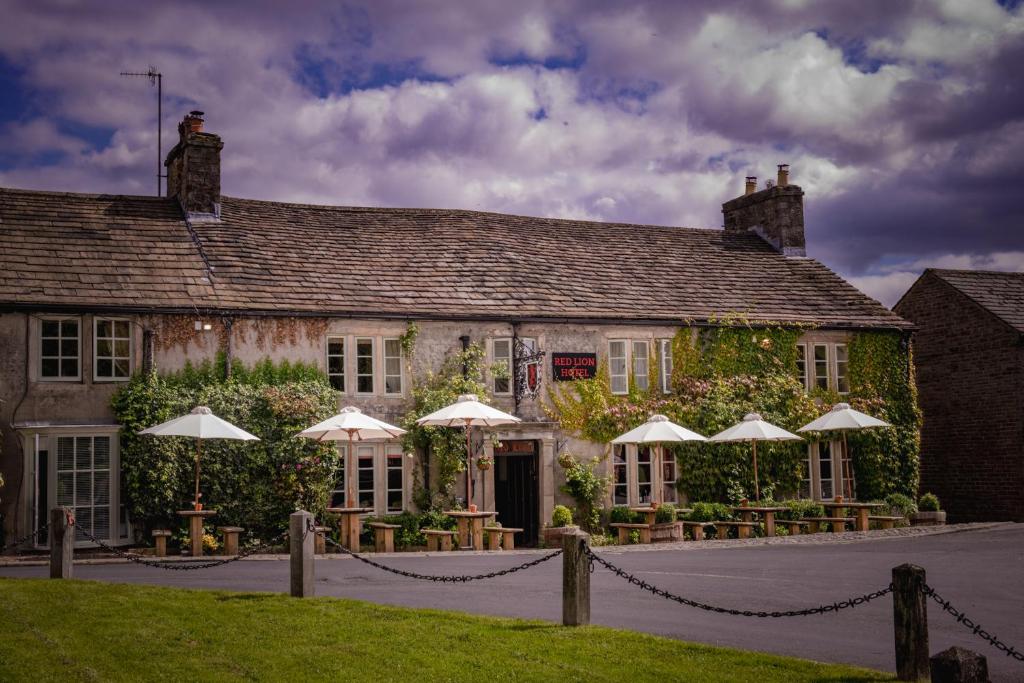 a building with tables and umbrellas in front of it at The Red Lion & Manor House in Burnsall