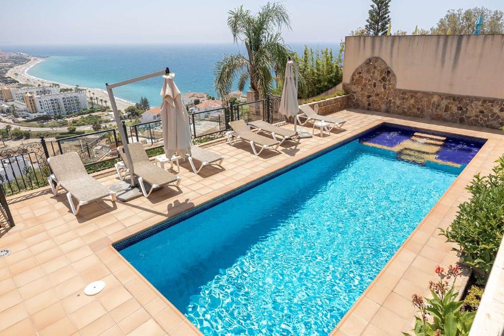 a swimming pool with chairs and umbrellas and the ocean at Vista Lara. Relájate y disfruta. in Nerja