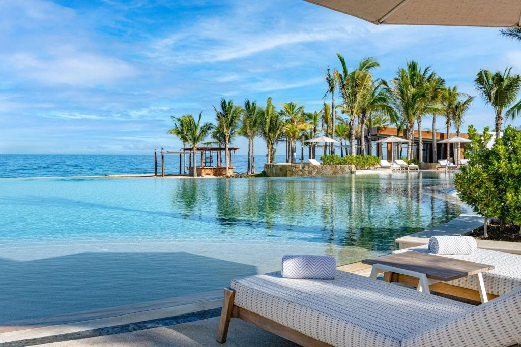 una piscina in un resort con palme e oceano di Conrad Punta de Mita a Punta Mita