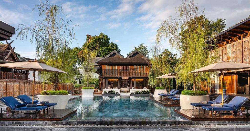a pool with chairs and umbrellas in front of a house at Aleenta Retreat Chiang Mai in Chiang Mai