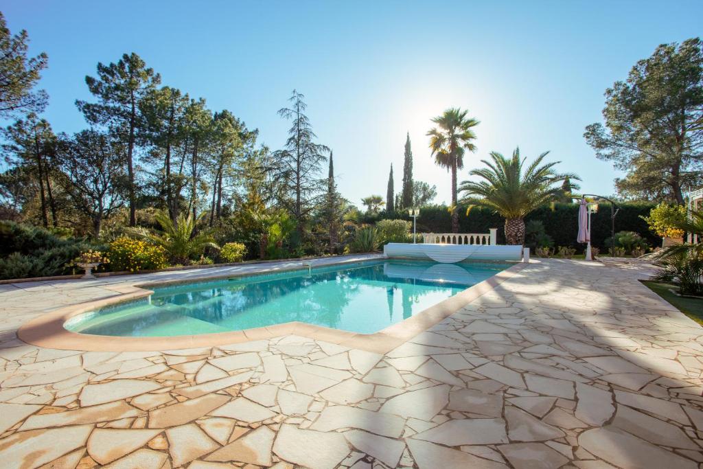 une piscine dans une cour arrière avec des arbres et des palmiers dans l'établissement Appartement - Clos Saint Jean, à Roquebrune-sur Argens