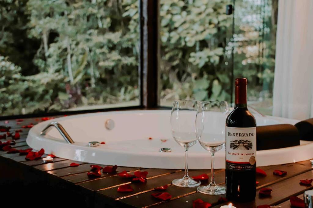 - Uma garrafa de vinho e 2 copos numa mesa com uma banheira; em Casa de campo em Joinville com Hidromassagem e Lareira em Joinville