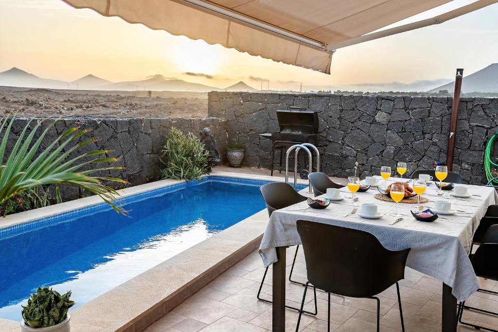 a dining table and chairs next to a swimming pool at Villa LanzaCosta Golf in Teguise