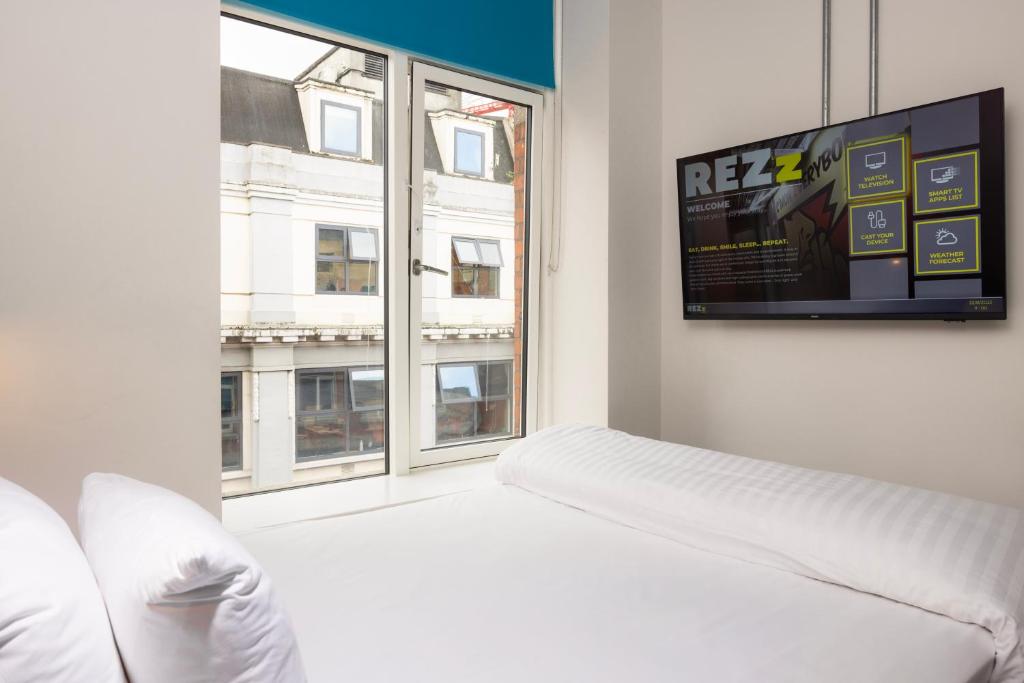 Hotel room with a bed, large window, and wall-mounted TV.