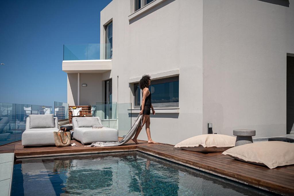 a woman walking on a deck next to a swimming pool at Alectrona Living Crete, Olīvea Luxury Apartment in Plataniás