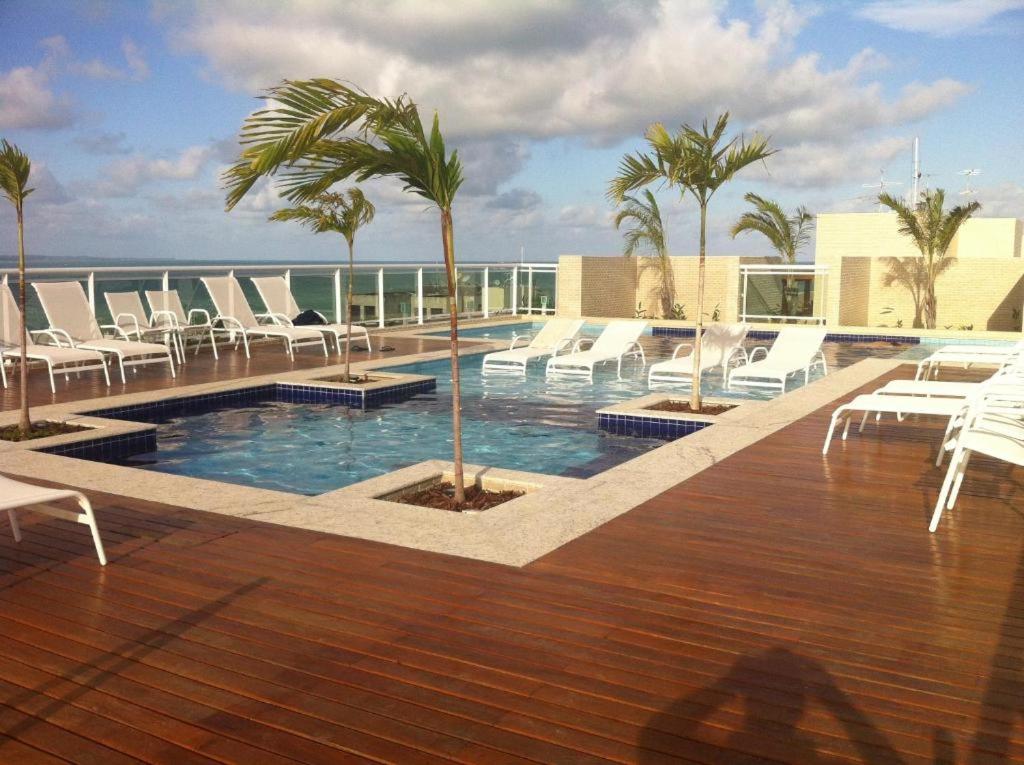 a swimming pool with chairs and palm trees on a building at Apartamento em Maceió a beira mar in Maceió