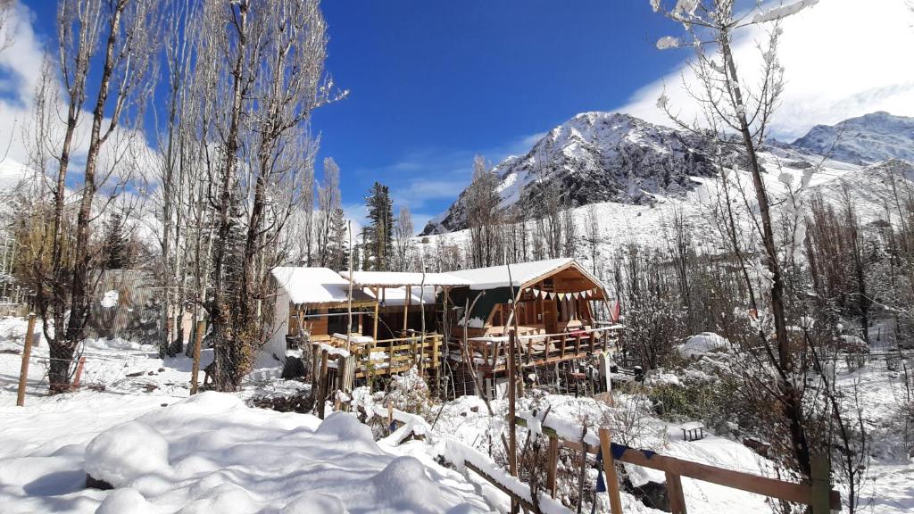 uma cabana de madeira na neve com montanhas ao fundo em Hostal Crisol em Refugio Lo Valdés